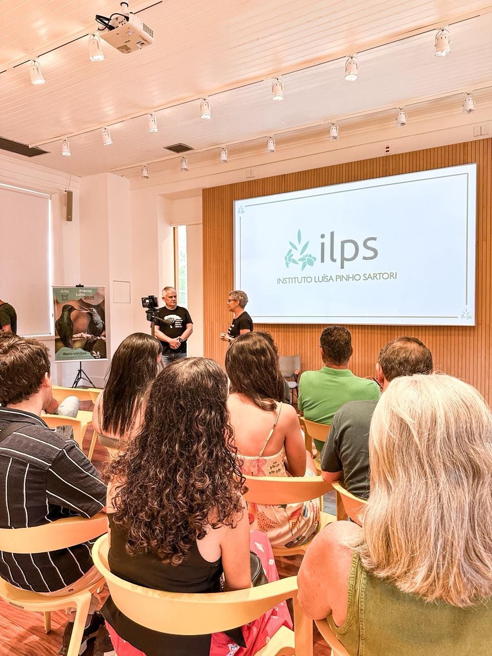 Um grupo de pessoas está sentado em uma sala de aula assistindo a uma apresentação.