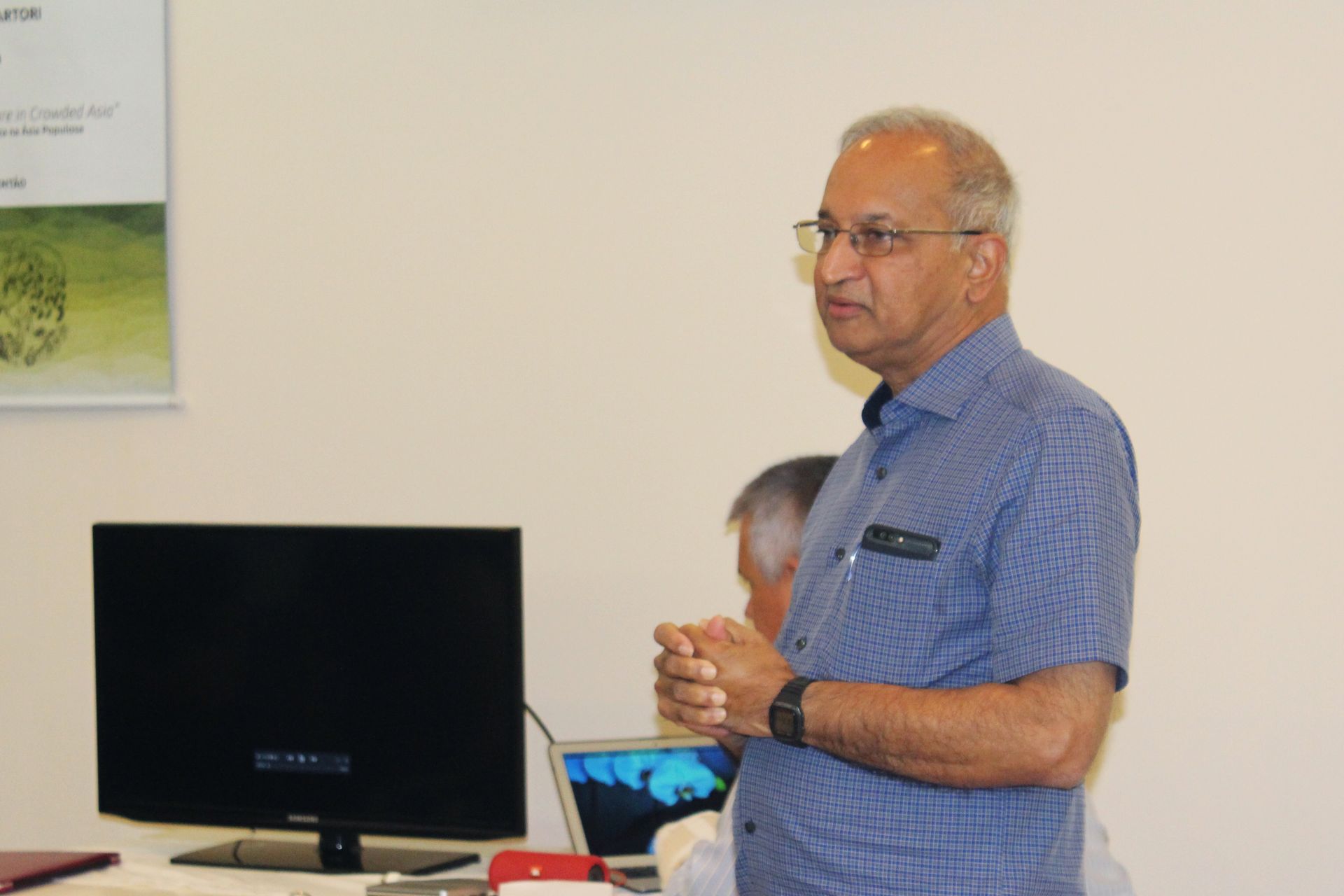 Um homem de camisa azul está parado em frente a um monitor de computador.