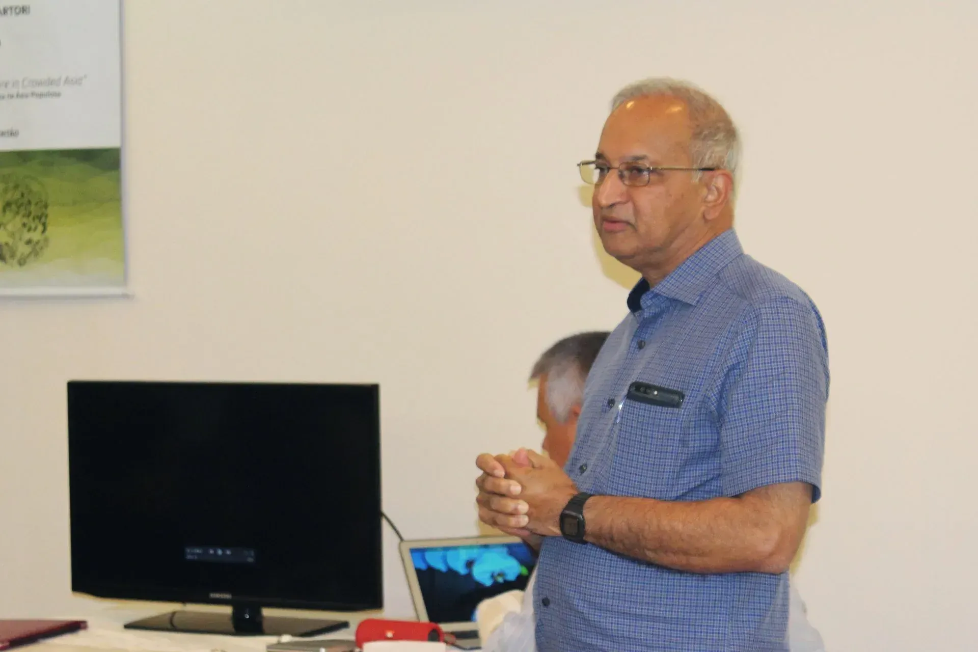 Um homem de camisa azul está parado em frente a um monitor de computador.