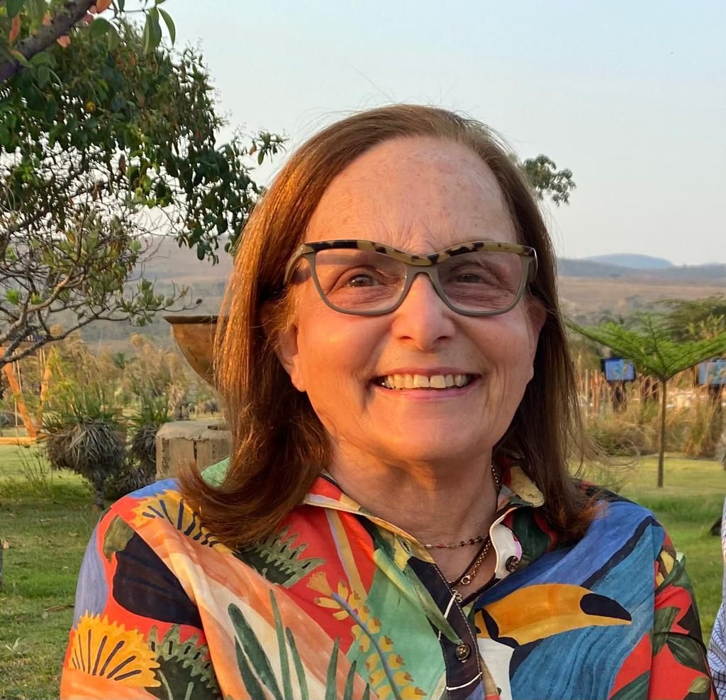 Uma mulher de óculos e uma camisa colorida está sorrindo para a câmera.