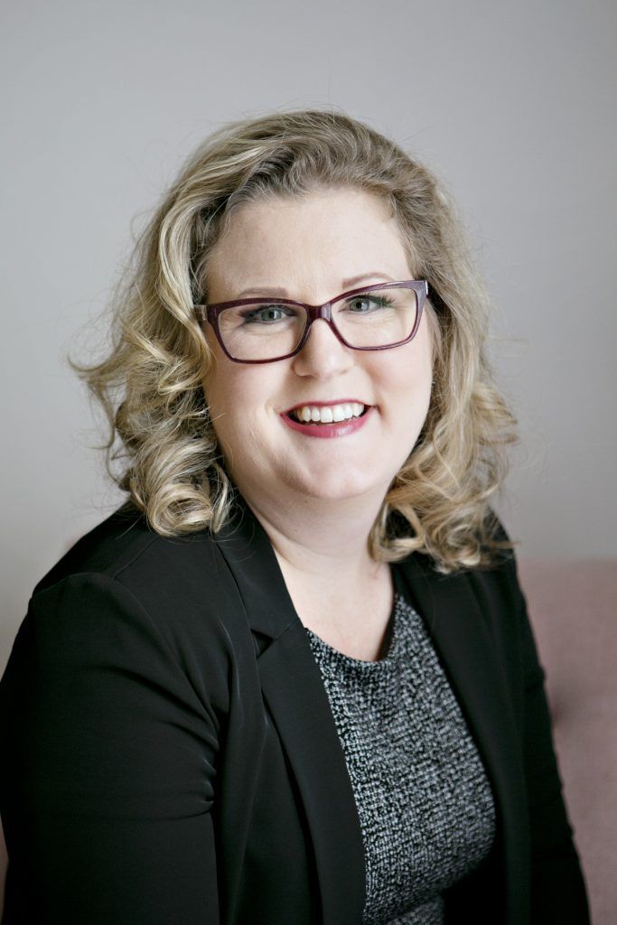 Smiling woman in glasses and a black blazer against a gray background