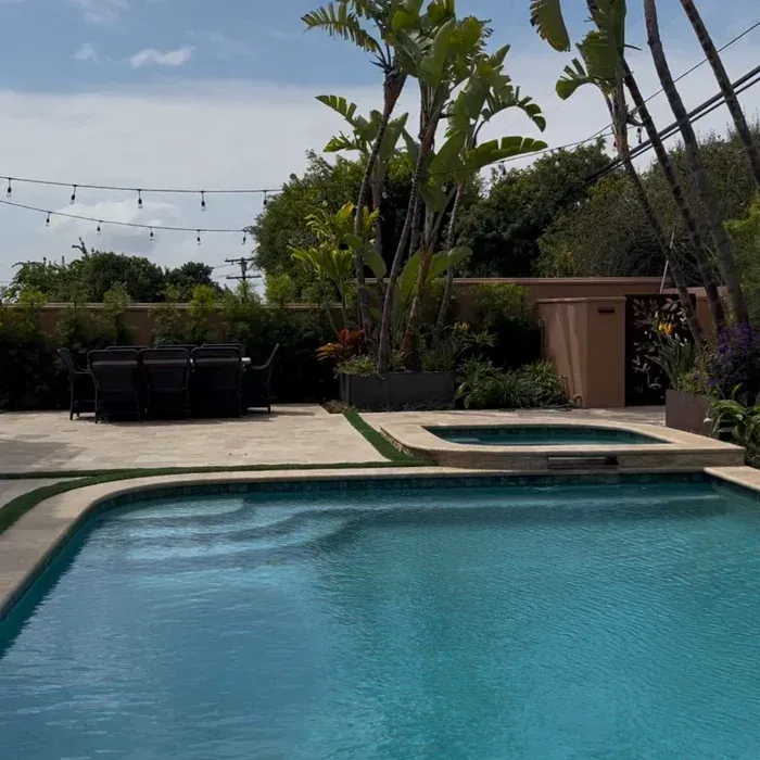 Backyard pool with patio seating, tropical plants, and string lights under a clear sky