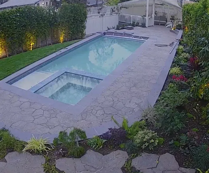 Backyard pool and hot tub at dusk, bordered by stone decking and lush landscaping