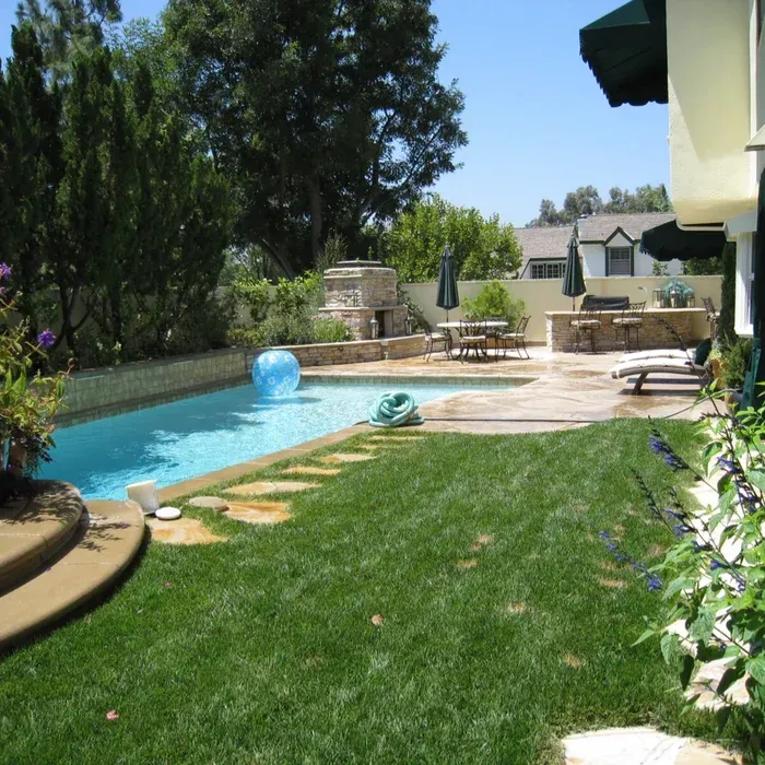 Backyard pool with lawn, stepping stones, patio furniture, and a blue float in sunny daylight