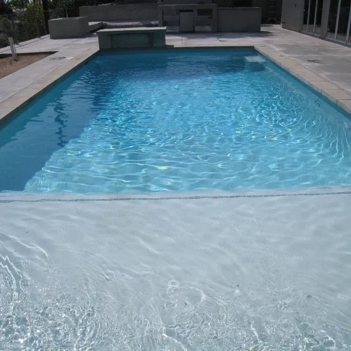 Blue backyard swimming pool with clear water and stone deck, viewed from the shallow end