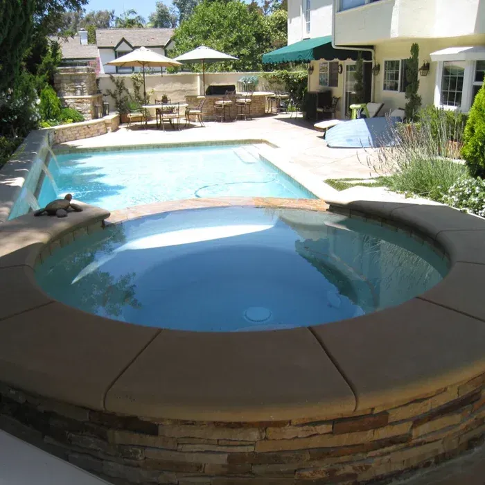 Backyard pool patio with a small round hot tub in front and lounge chairs by the main swimming pool