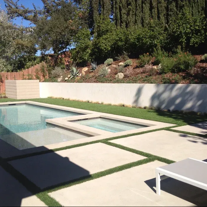 Modern backyard pool with geometric steps, white patio, lounge chair, and landscaped wall garden