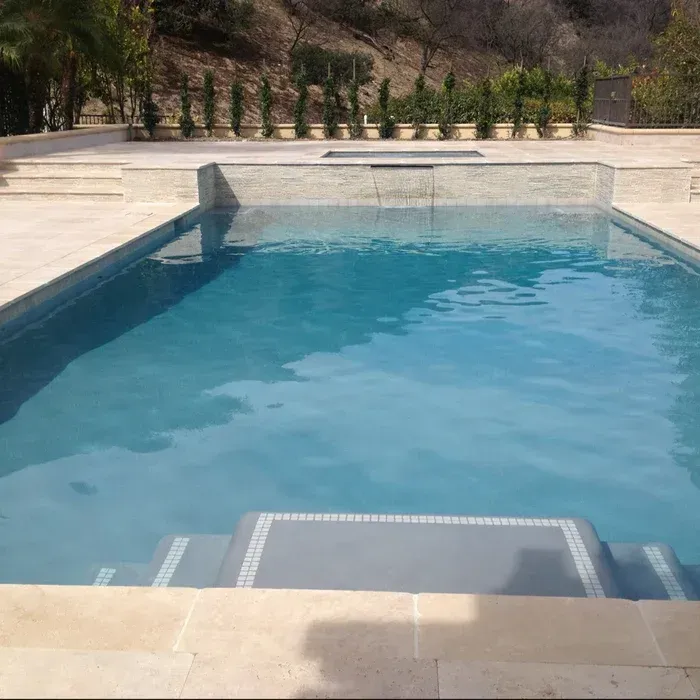 Backyard swimming pool with clear blue water and stone deck, viewed from the shallow end