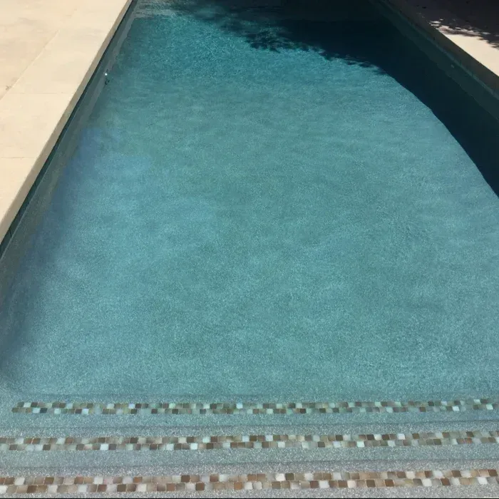 Blue swimming pool water bordered by pale stone decking and tiled steps at the near edge