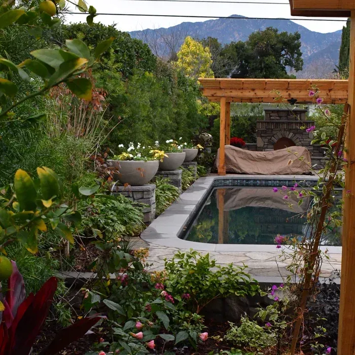 Lush garden patio with a small pool, potted plants, and mountain view in the background