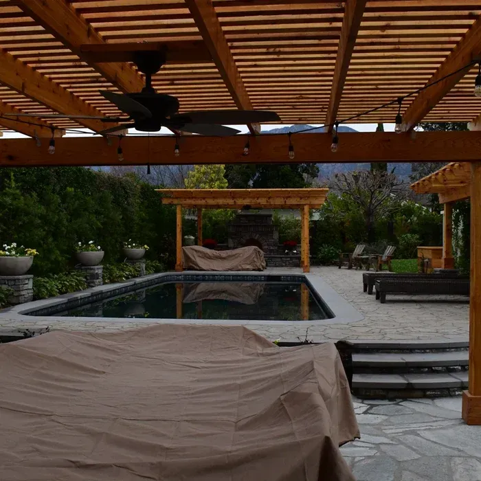 Covered patio with a pool, pergola seating, and furniture draped in tan protective covers