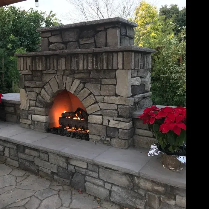 Stone outdoor fireplace with a glowing fire and red poinsettias on the right