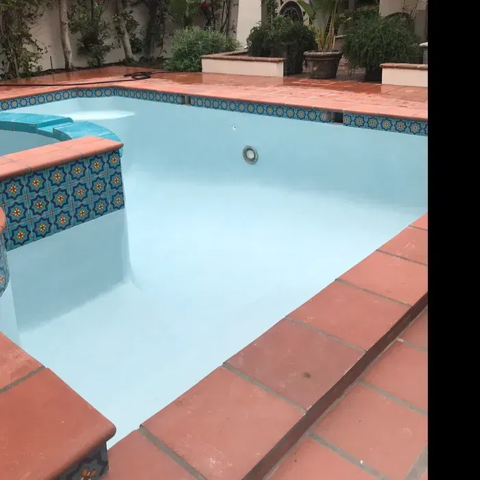 Empty tiled swimming pool with light blue interior and terracotta coping in a courtyard garden