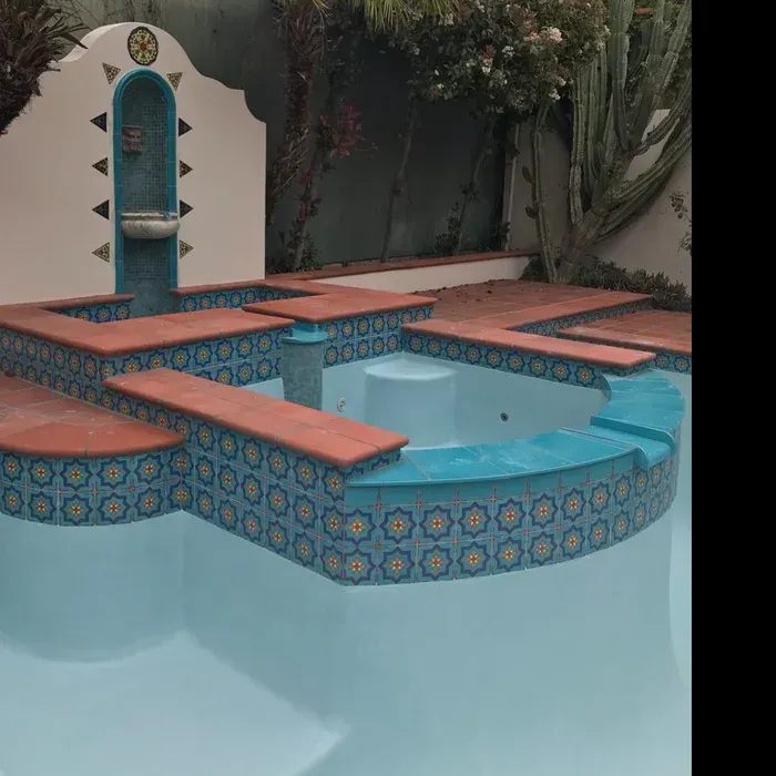 Tiled backyard pool with blue water, terracotta steps, and a small decorative fountain wall