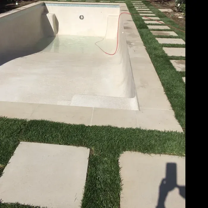 Empty white swimming pool beside a green lawn and stone walkway, with a hose draped inside.