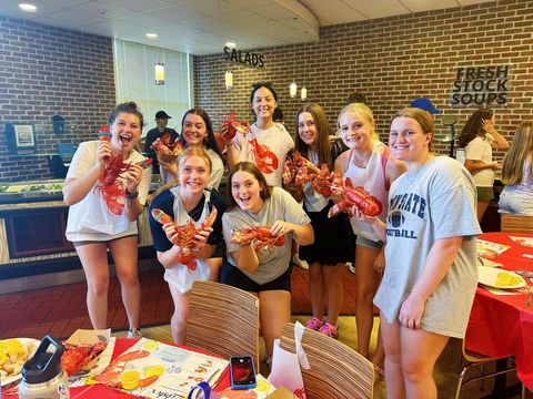A group of people standing in a restaurant, smiling and holding up fresh lobsters for the camera.