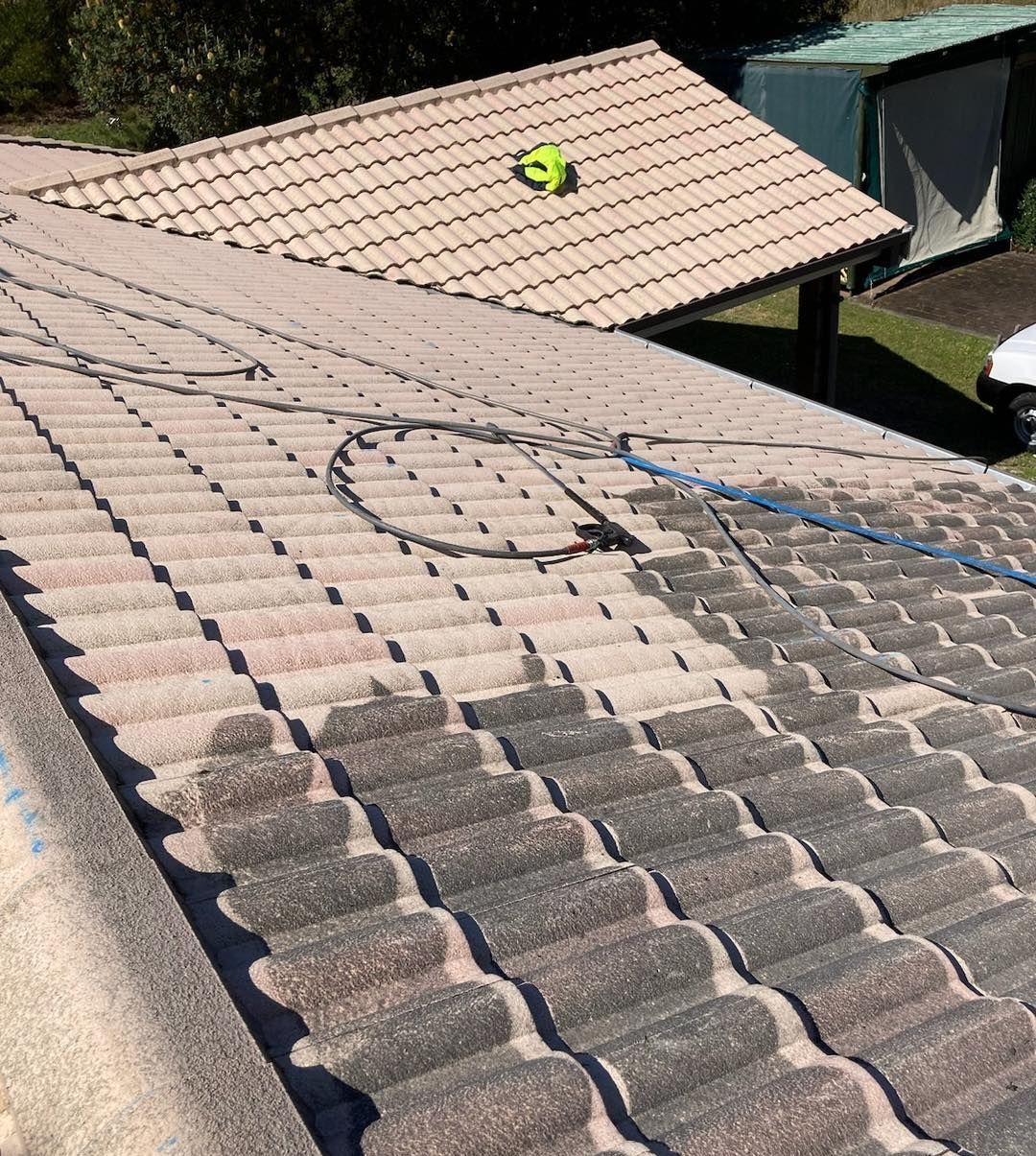A Man is Cleaning the Roof of a House With a High Pressure Washer — Wayne Treasure Roofing & Restoration In Forster, NSW