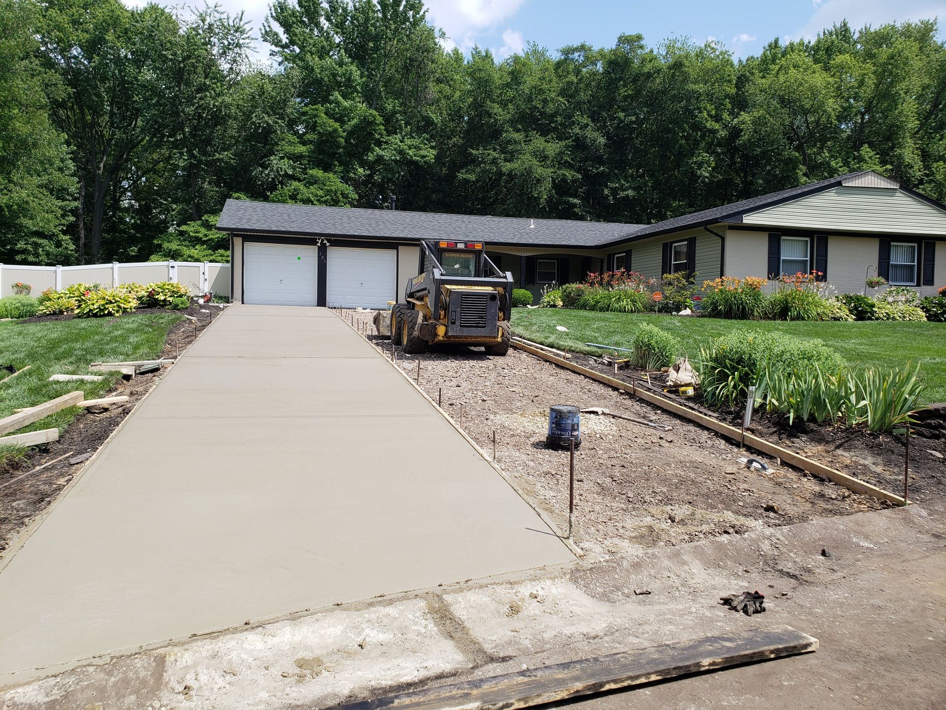 Driveway under construction leading to a house with a garage and garden beds.