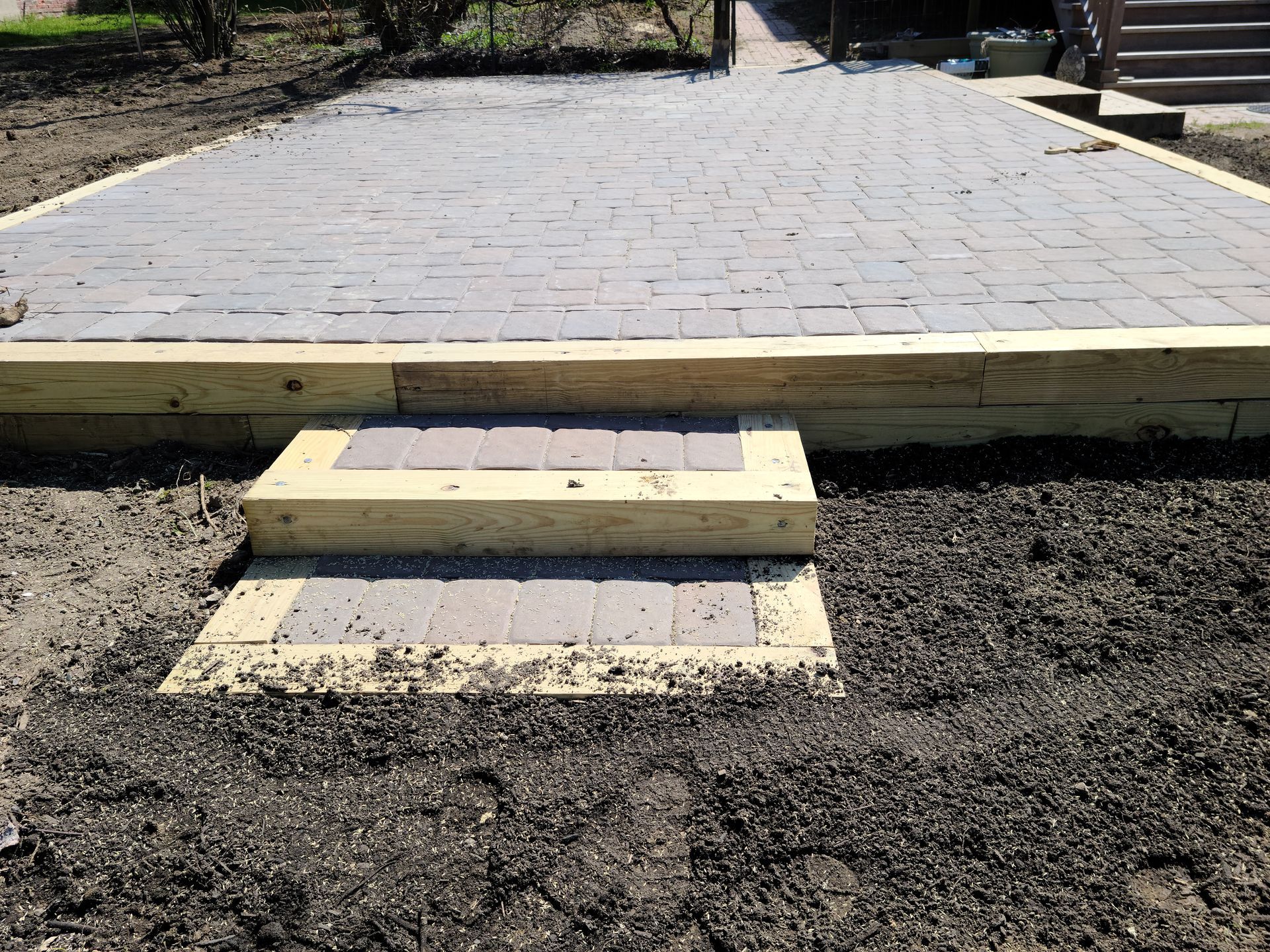 Paved walkway with concrete steps leading up from a dirt area, outdoors in daylight
