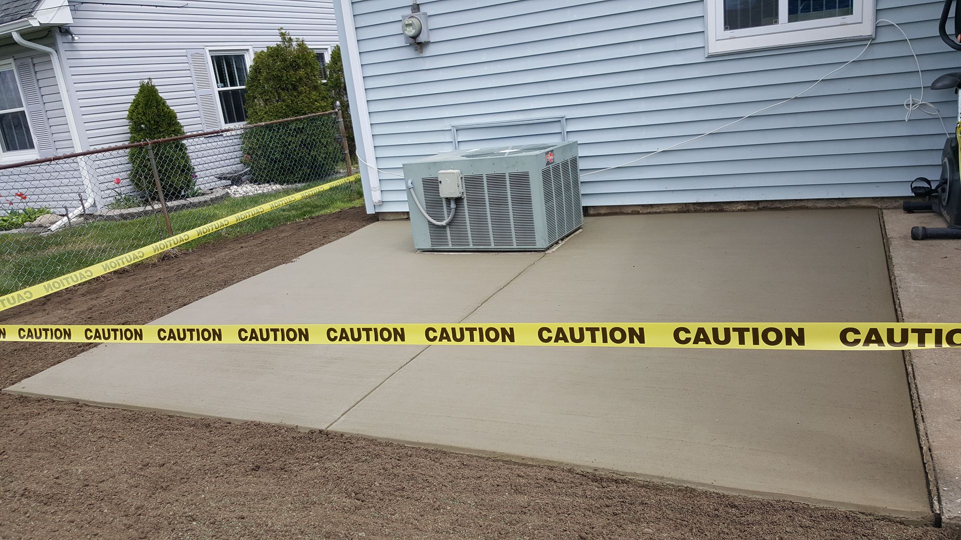 Caution tape cordons off a concrete walkway beside a house and air conditioner unit.
