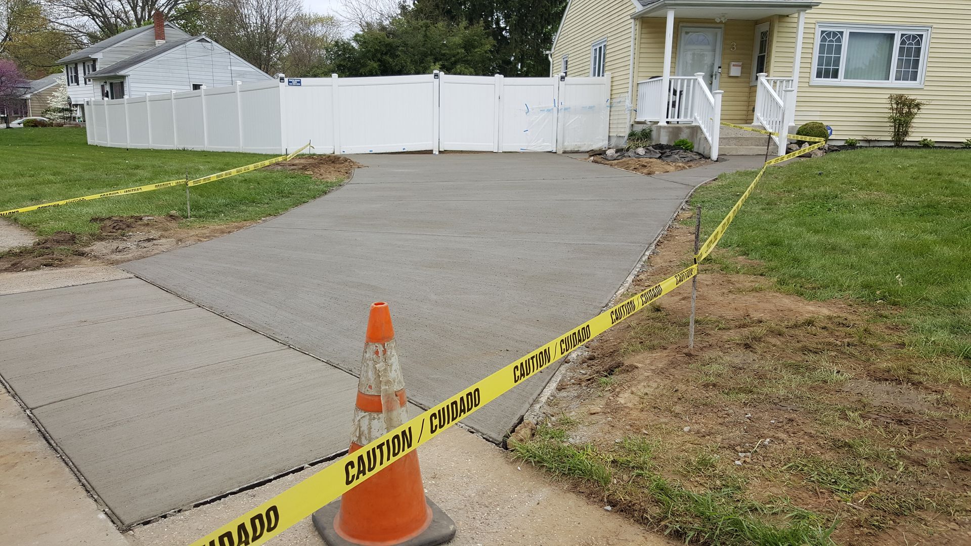 Freshly poured concrete driveway blocked by caution tape and an orange cone beside a house