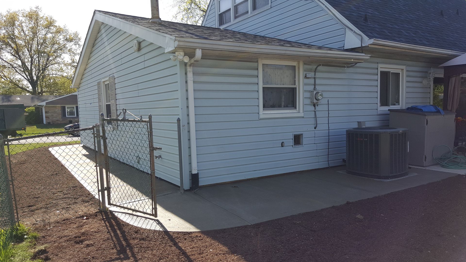 White house side yard with chain-link fence, gravel path, and air-conditioning units near the wall