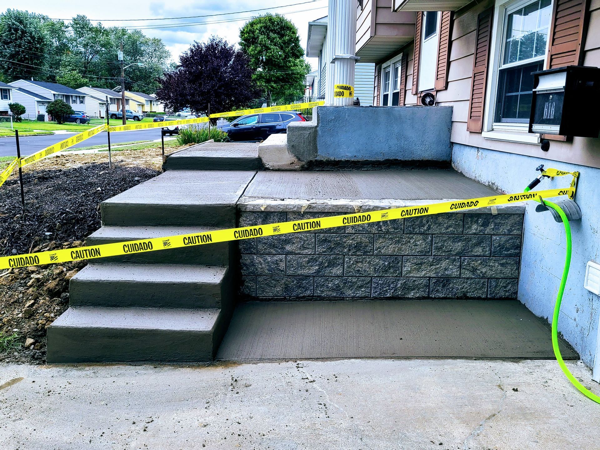 Caution tape blocks a front porch with concrete steps and a ramp, indicating construction or repair work.