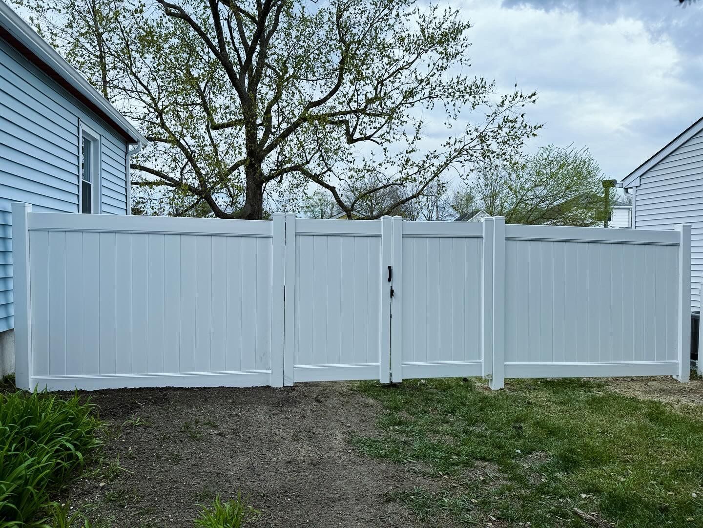 White vinyl fence and gate between two houses beside a gravel driveway under a cloudy sky