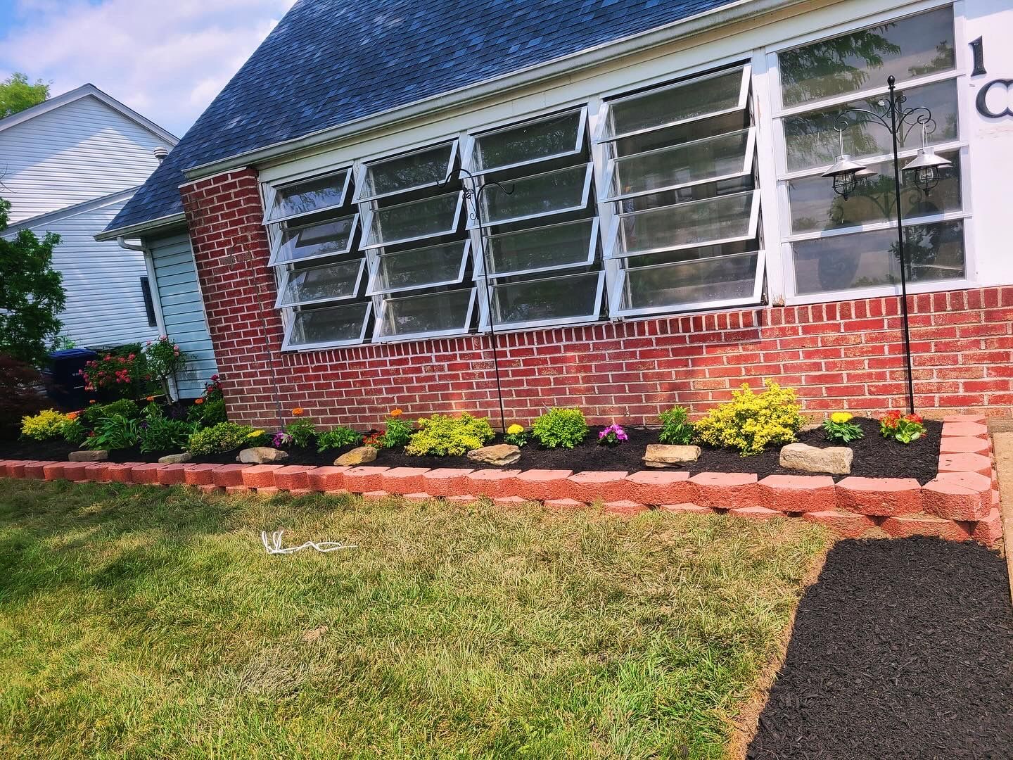 Brick house exterior with large windows, flower bed, and green lawn