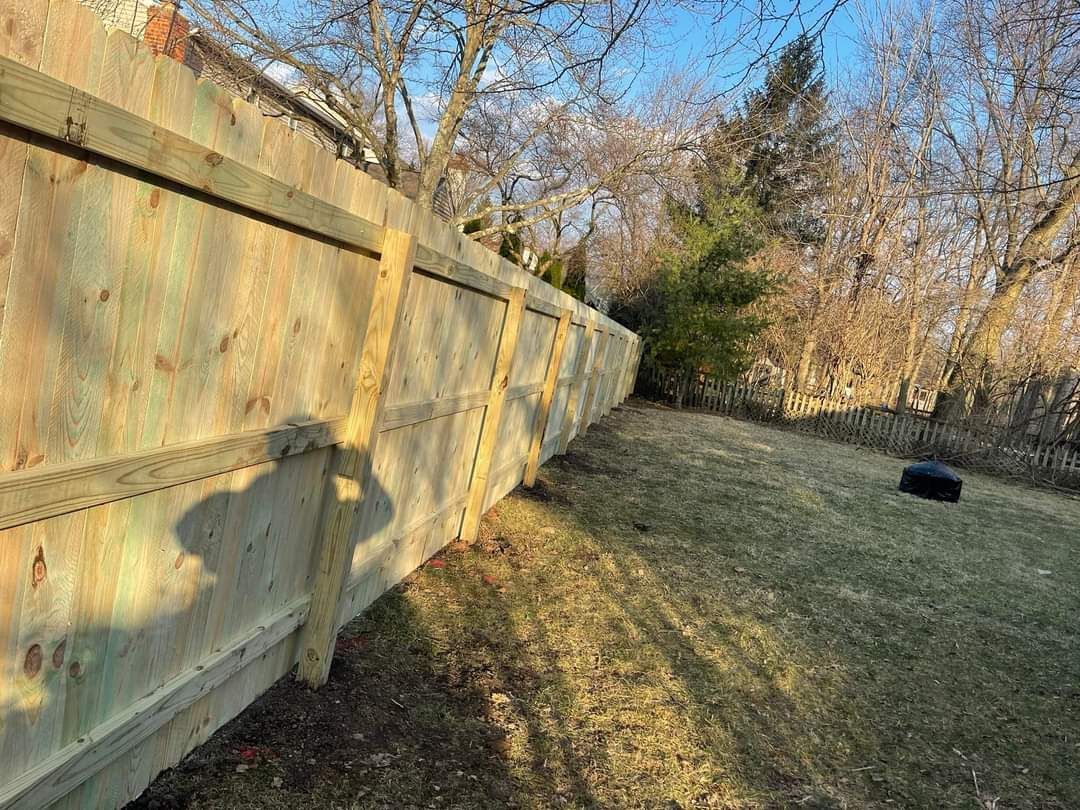 Long concrete wall beside a grassy field with trees and a black tire under a clear blue sky
