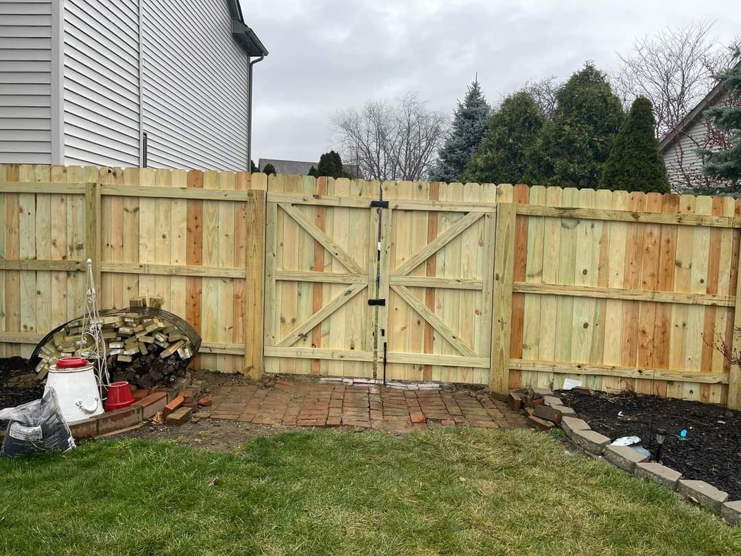 Backyard with a wooden privacy fence, grass lawn, and a small stone patio under construction.