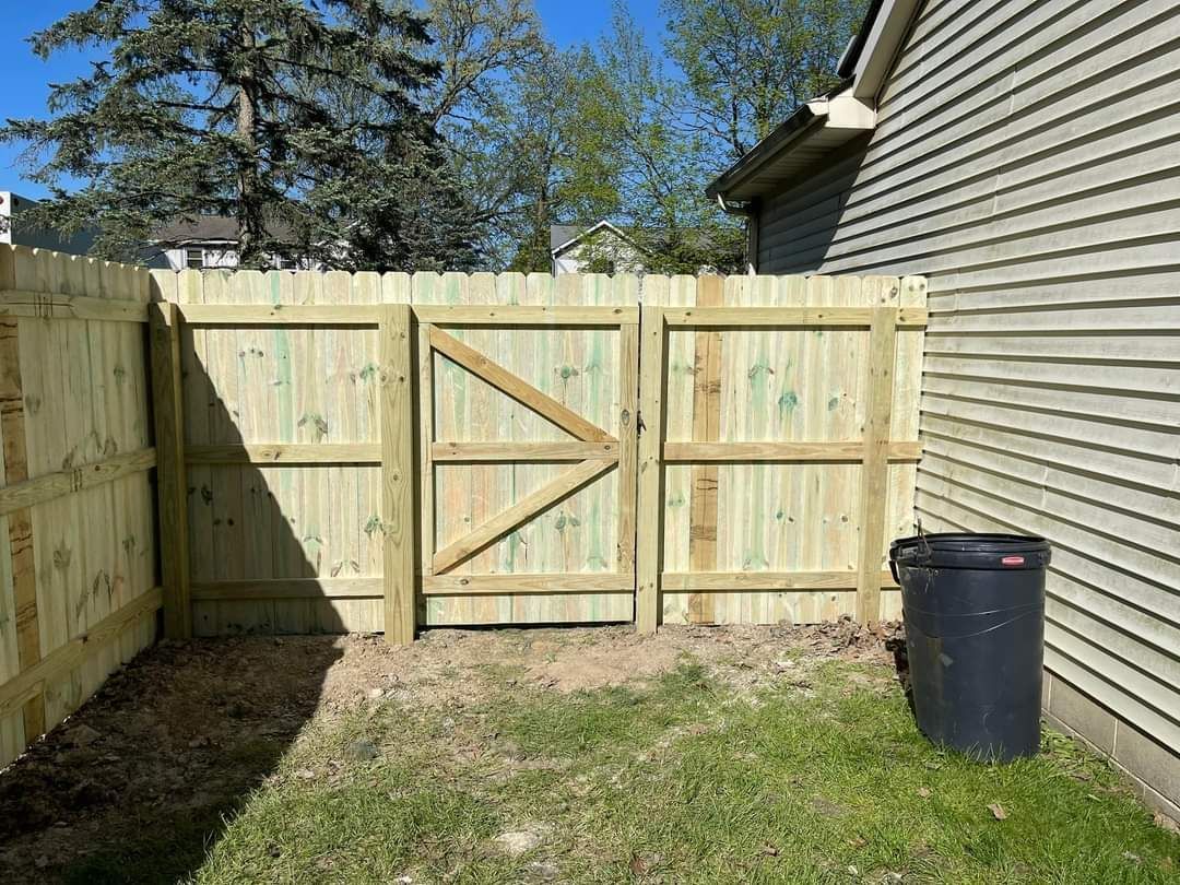 Backyard corner with a new wooden privacy fence and gate beside a house and trash bin.