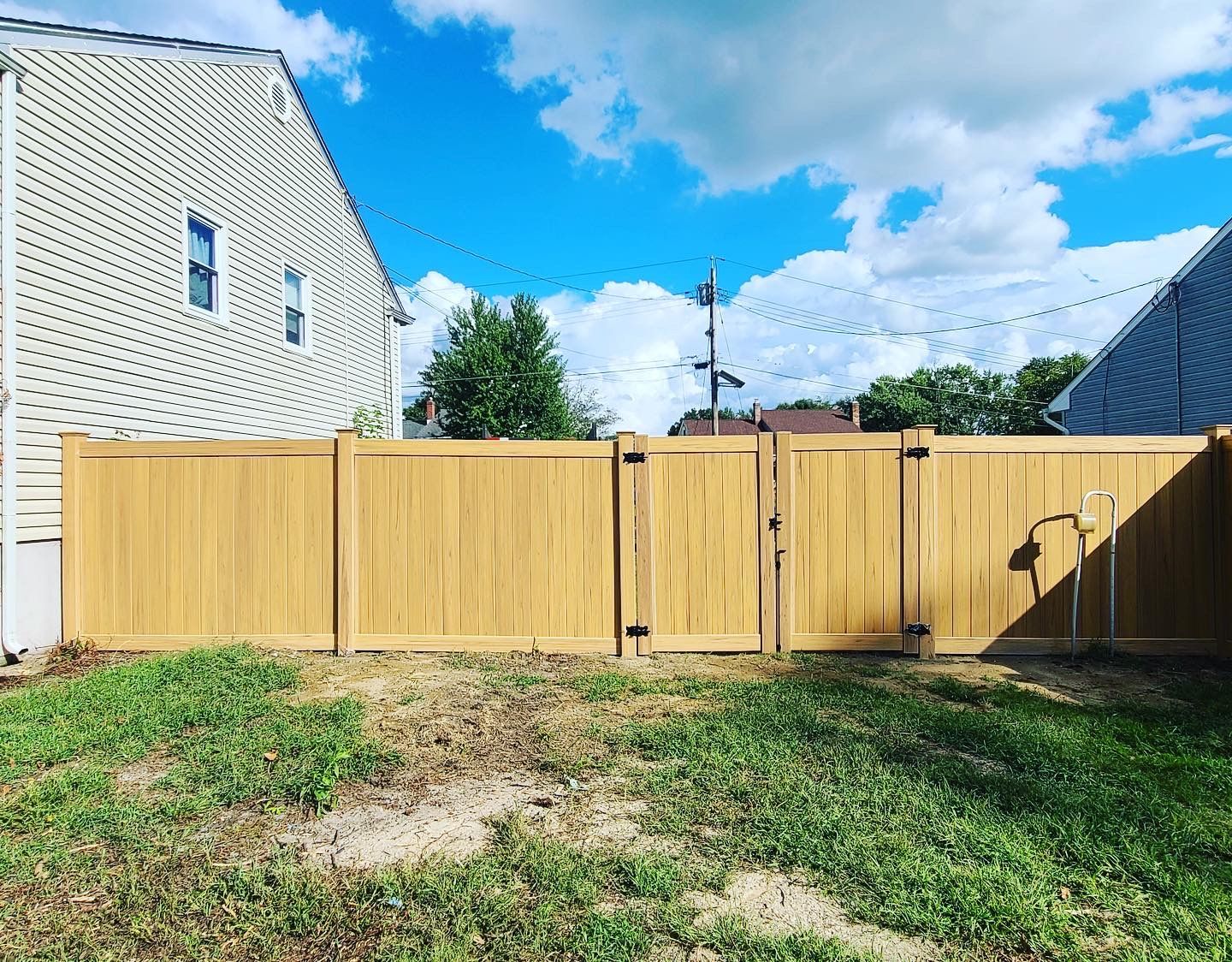Wooden backyard fence and gate in a grassy yard beside a white house under a blue sky