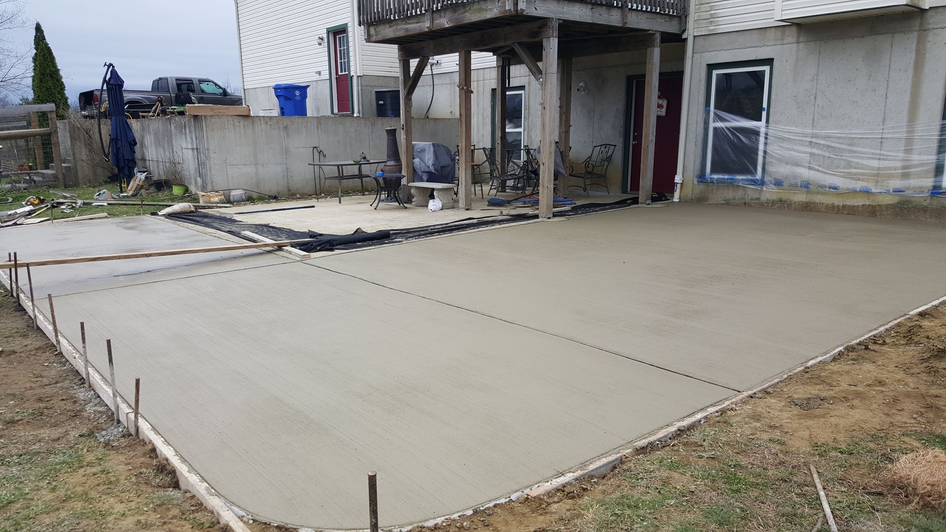 Freshly poured concrete patio beside a house under construction, with foundation walls and support posts.