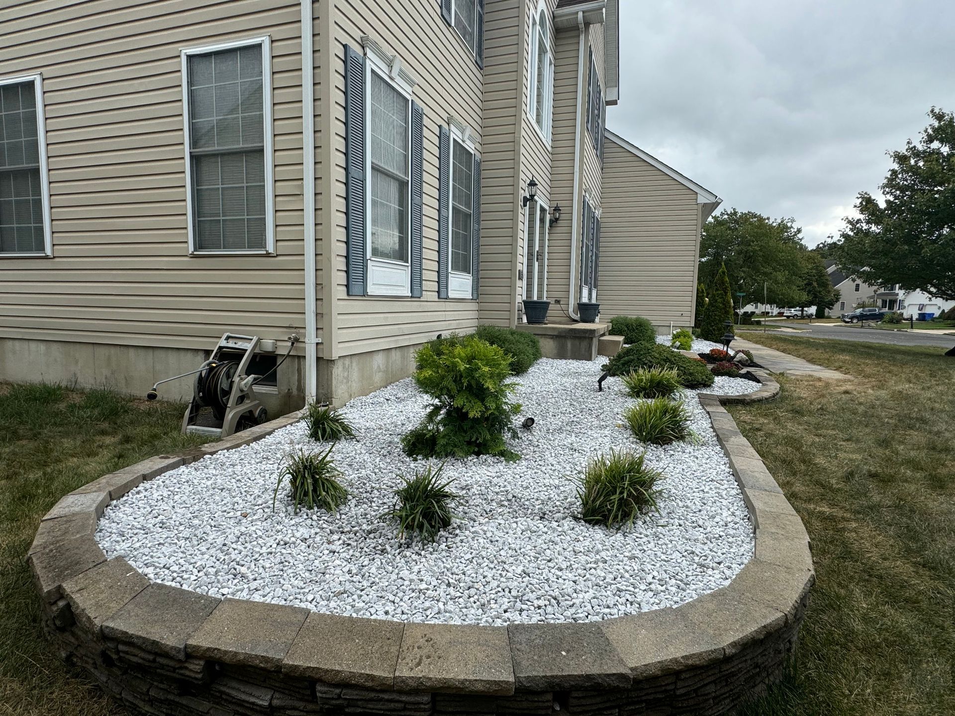 Landscaped corner bed with white stone mulch and small shrubs beside a beige house