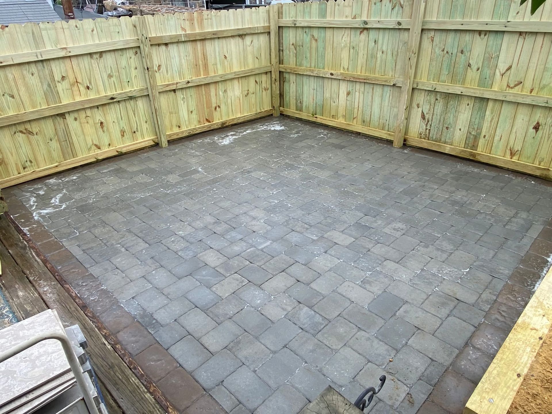Empty paved backyard patio enclosed by wooden fencing