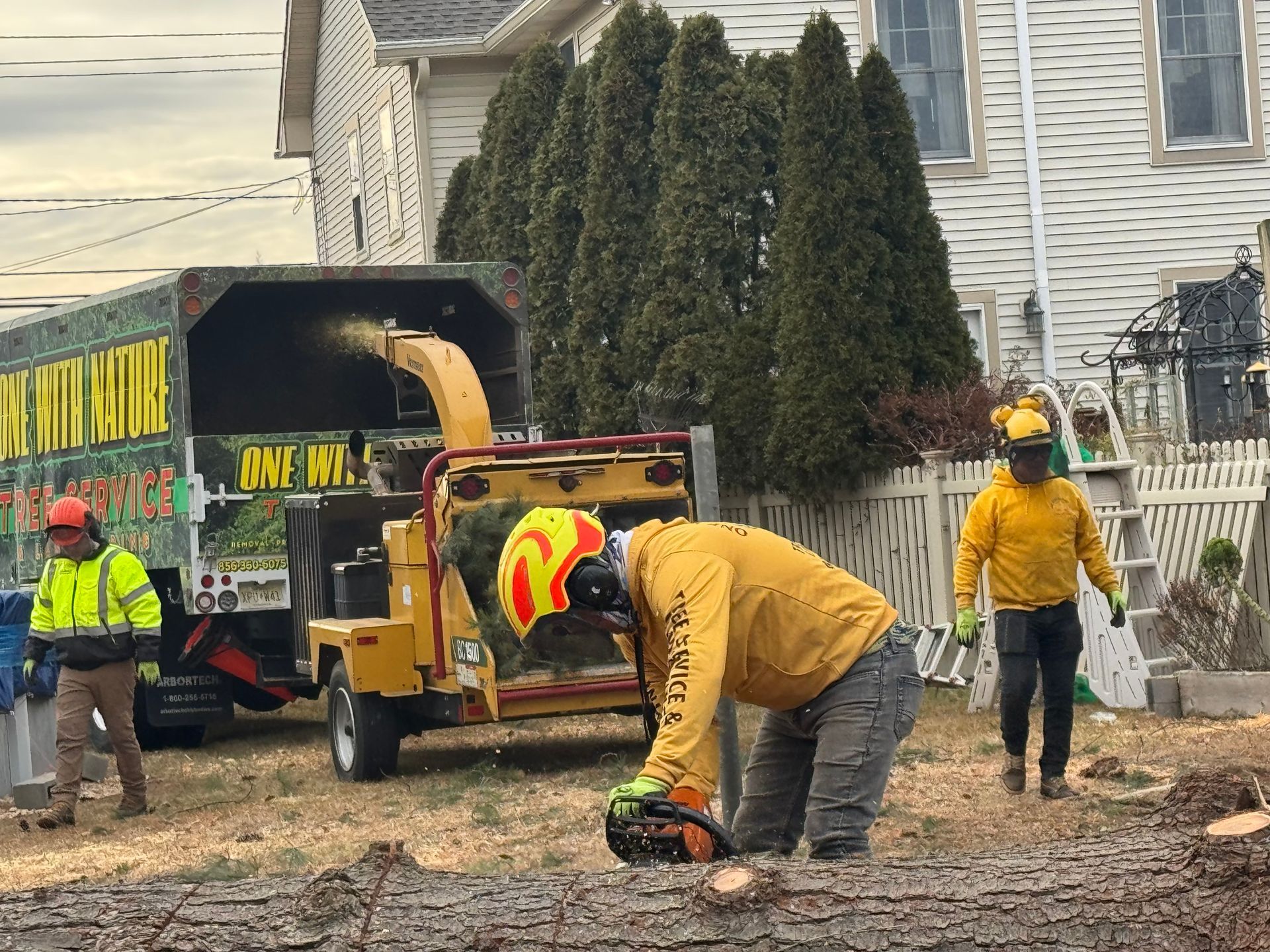 Road crew using a chainsaw near a yellow dump truck in a residential yard