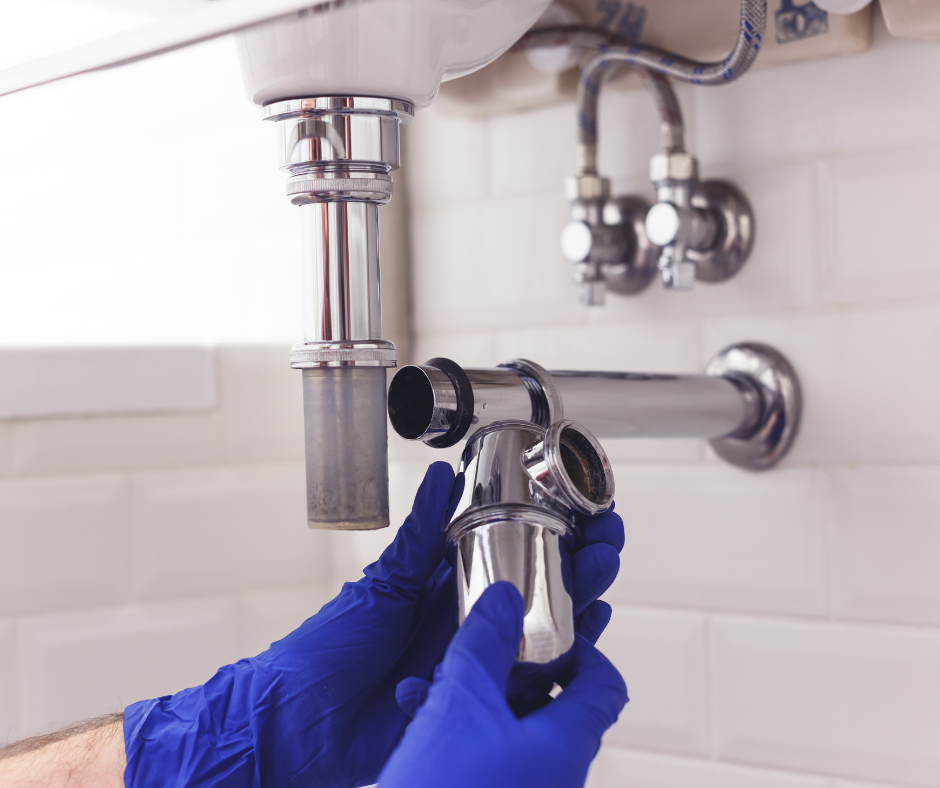 Gloved hands installing a chrome sink faucet under a bathroom sink