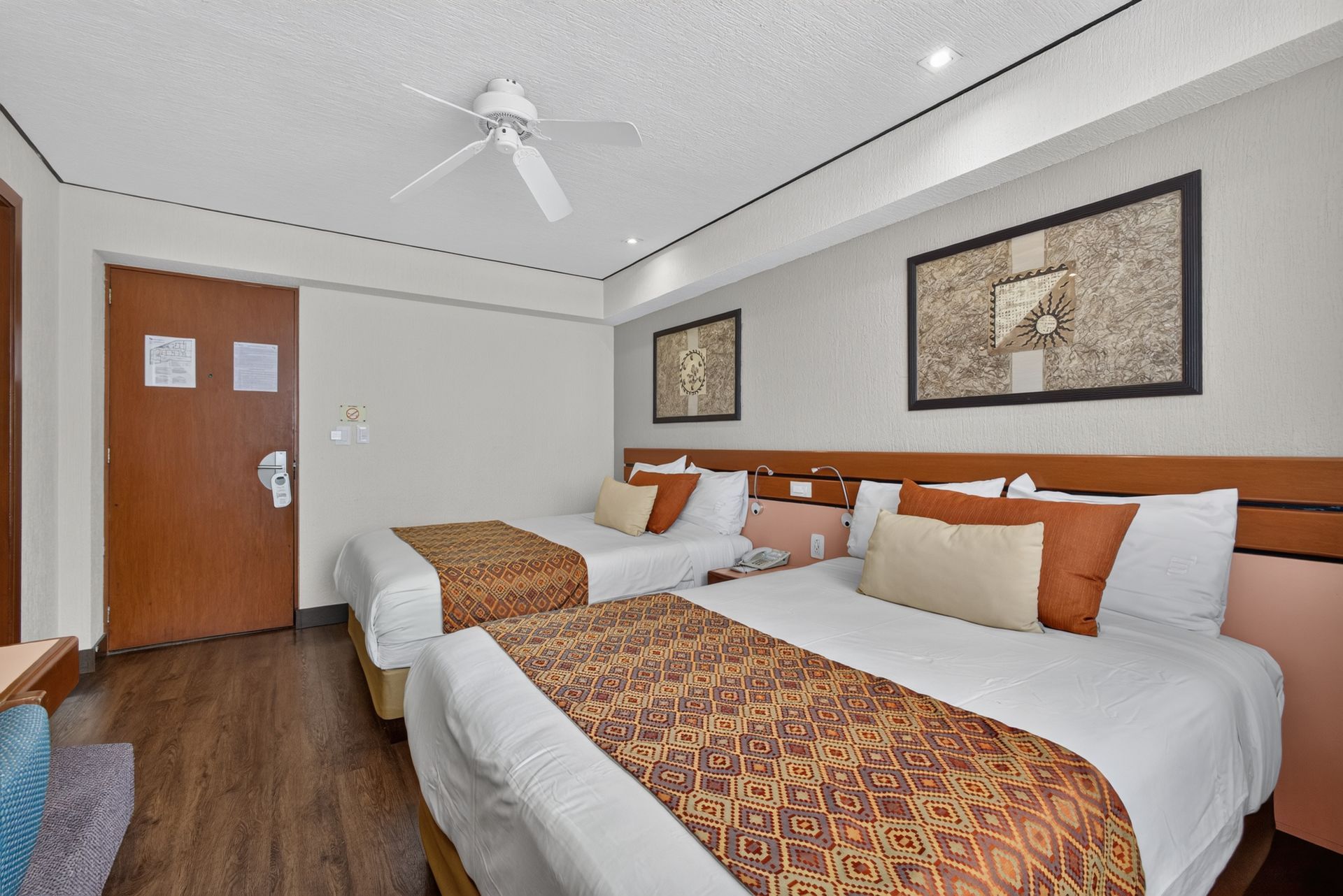 Habitación de hotel con dos camas individuales, paredes de madera cálida, TV, escritorio y cortinas luminosas.