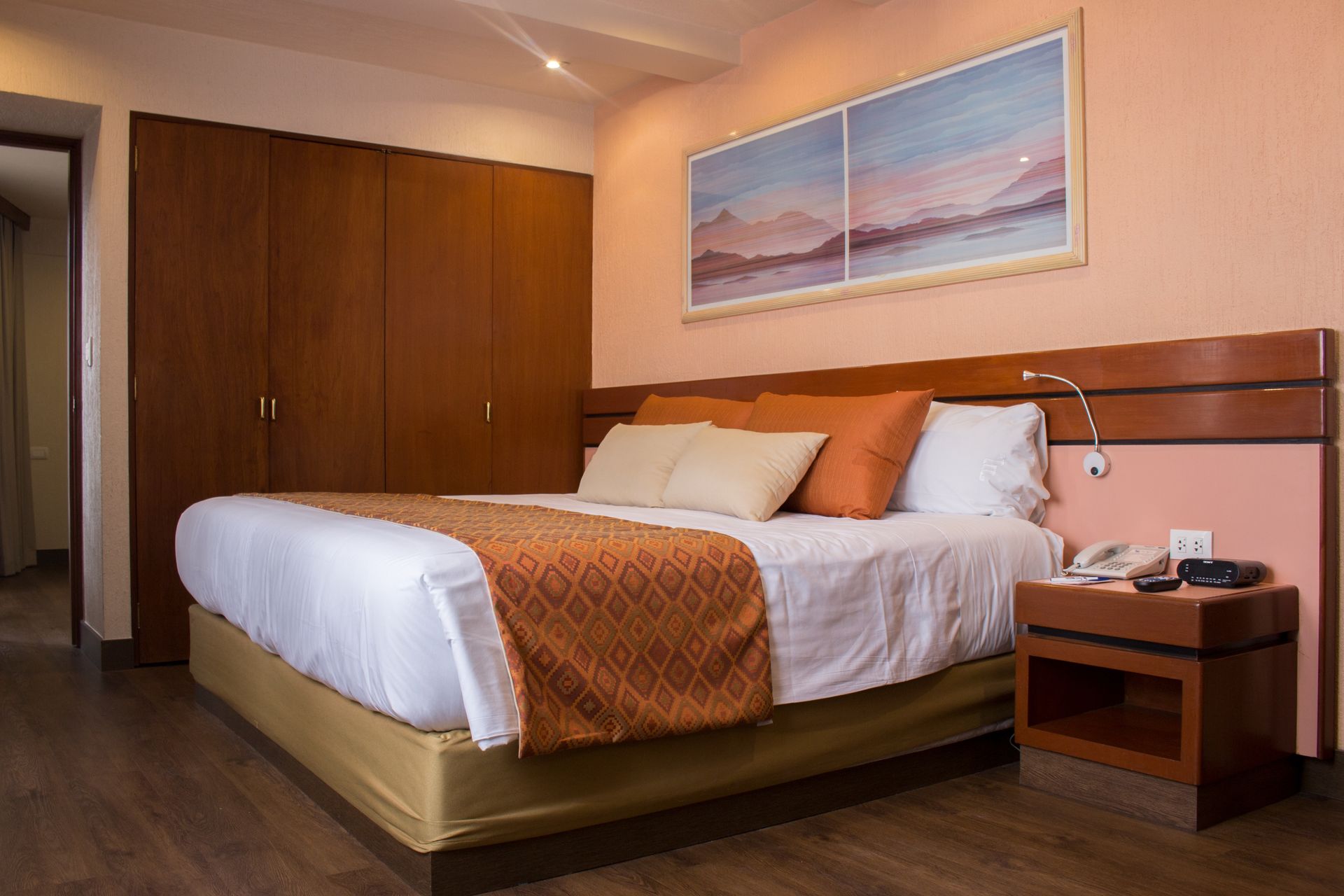 Habitación de hotel moderna con una cama bien hecha, mesita de noche, cortinas y cuadros enmarcados.