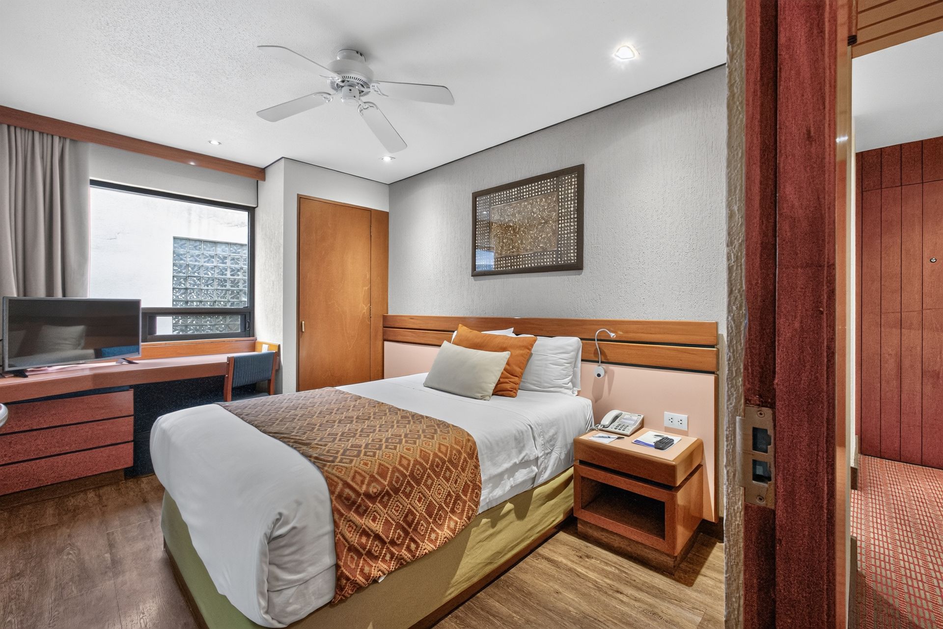 Habitación de hotel moderna con una cama bien hecha, cabecero de madera, escritorio, ventana y cuadros enmarcados en la pared