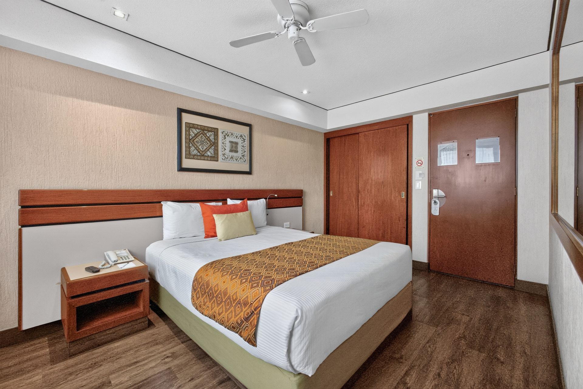Acogedora habitación de hotel con una cama bien hecha, cabecero de madera, escritorio y una gran ventana.