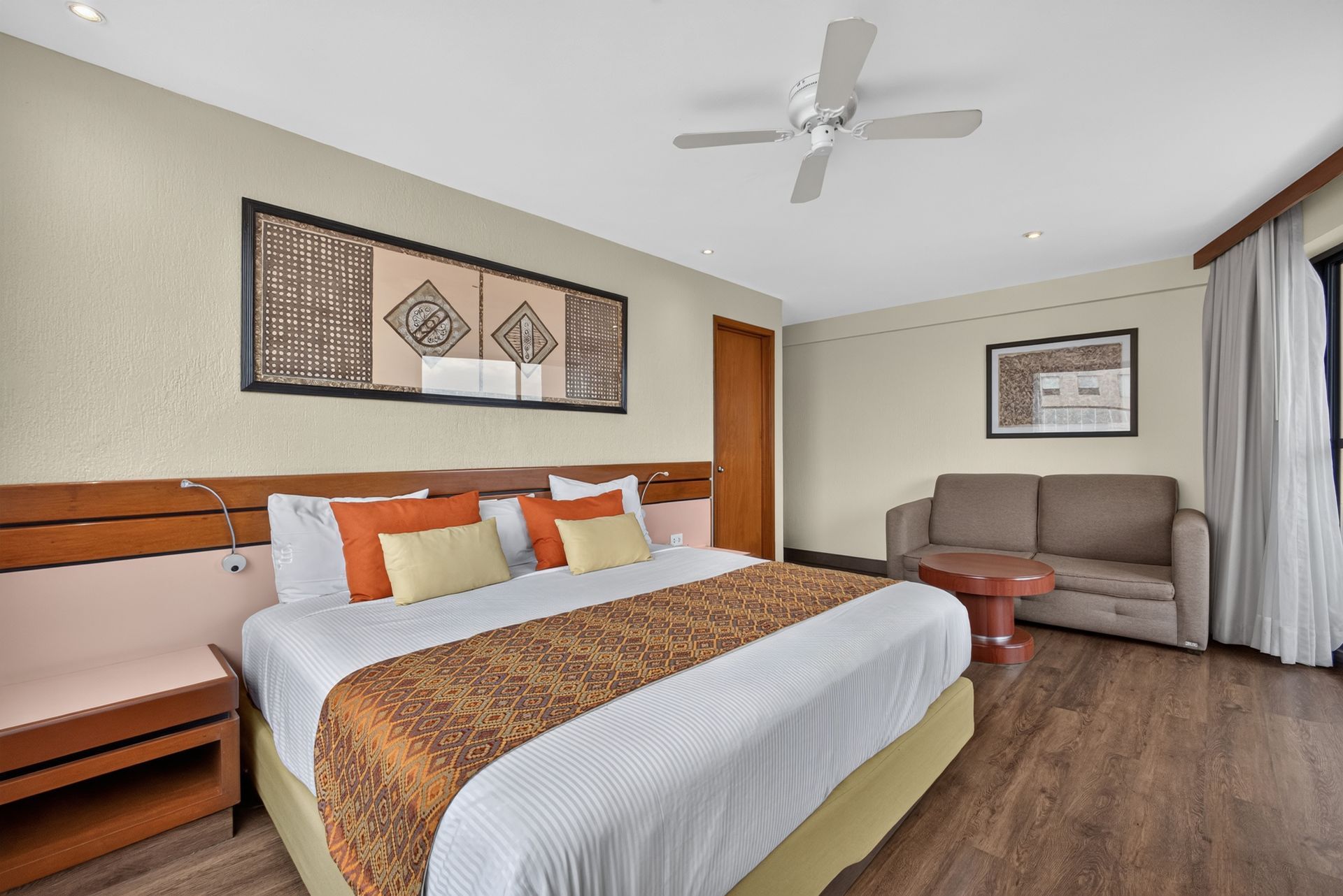 Habitación de hotel con cama king size, ropa de cama blanca, detalles en color tostado y un paisaje marino.