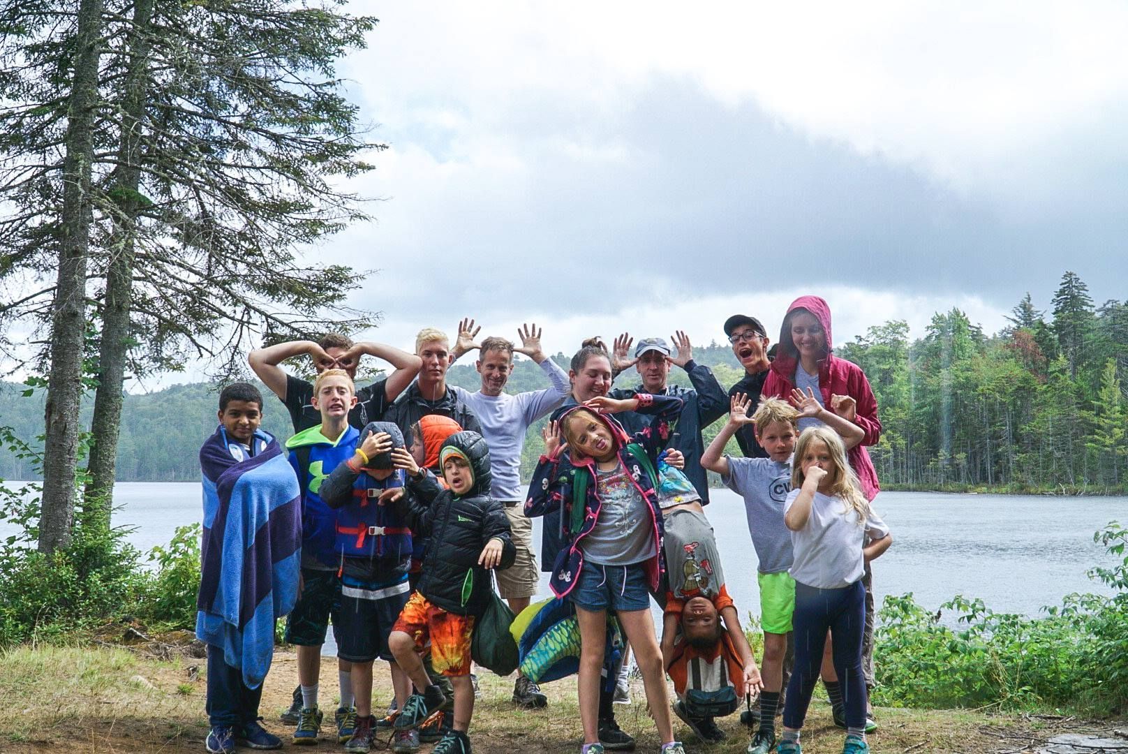 a group of children are posing for a picture in front of a lake .