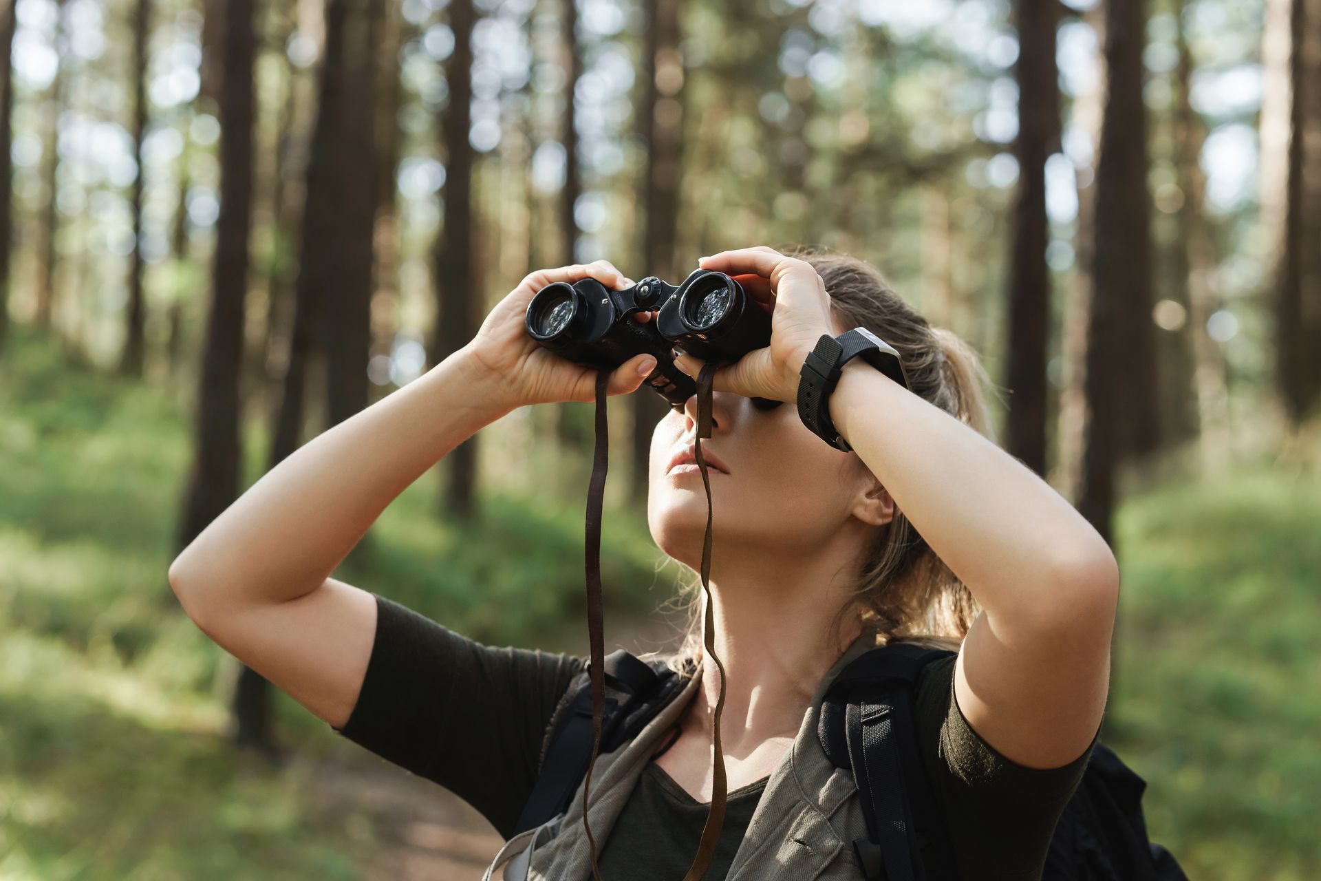 A woman is looking through binoculars in the woods.