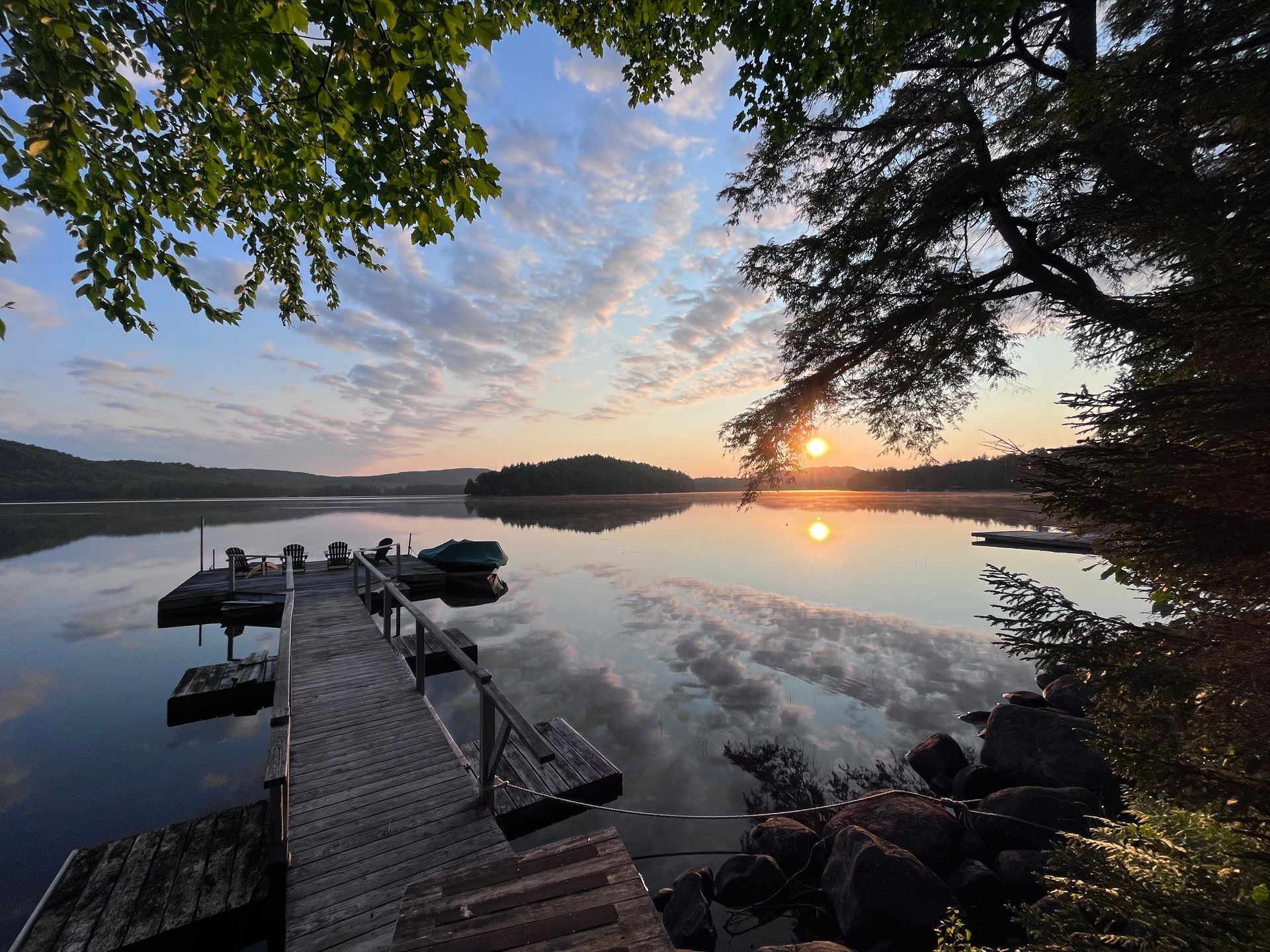 the sun is setting over a lake with a dock in the foreground