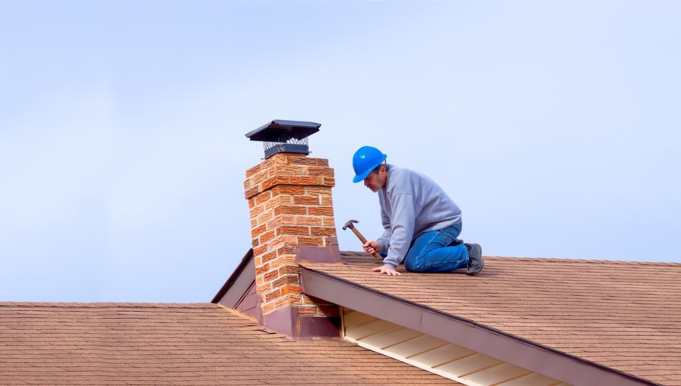 Worker in blue hard hat repairing a rooftop chimney on a shingled roof