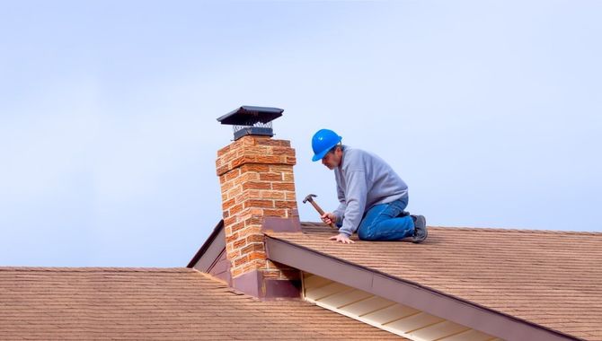 Worker in a blue hard hat repairing a brick chimney on a shingled roof