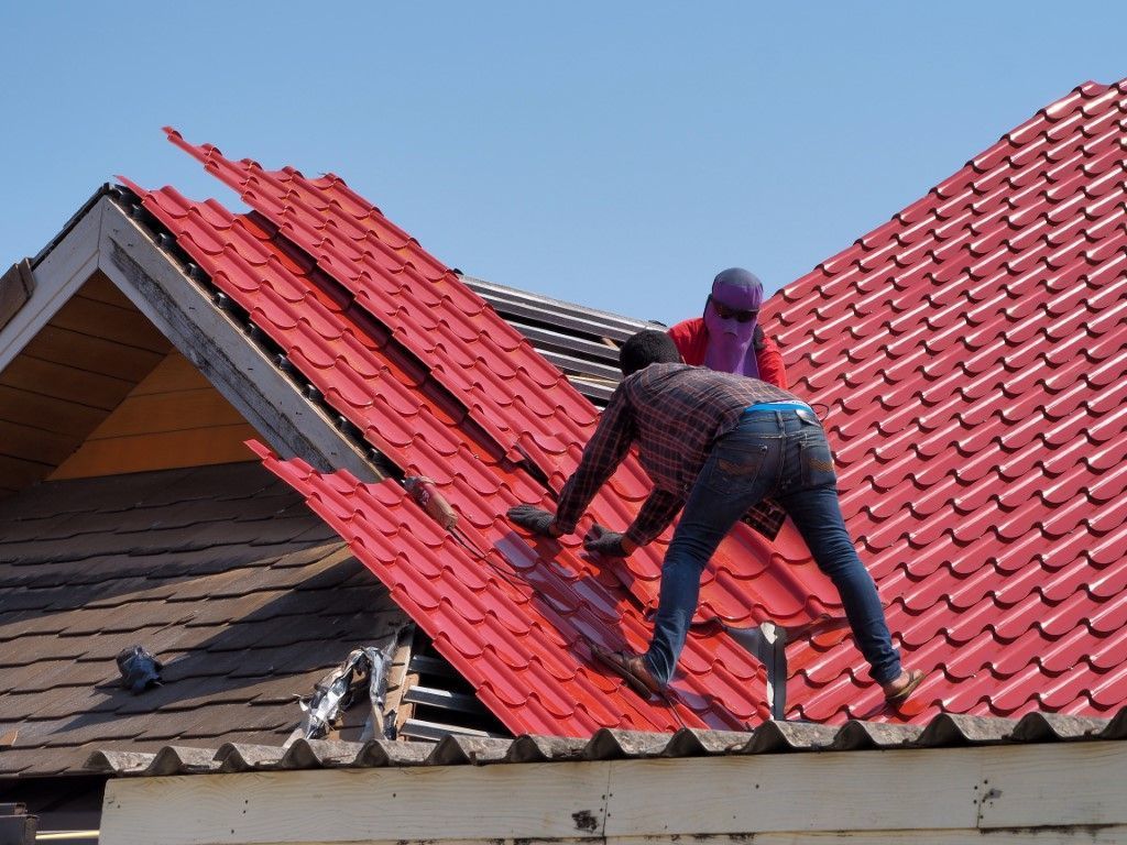 Two workers installing red roof tiles on a house roof