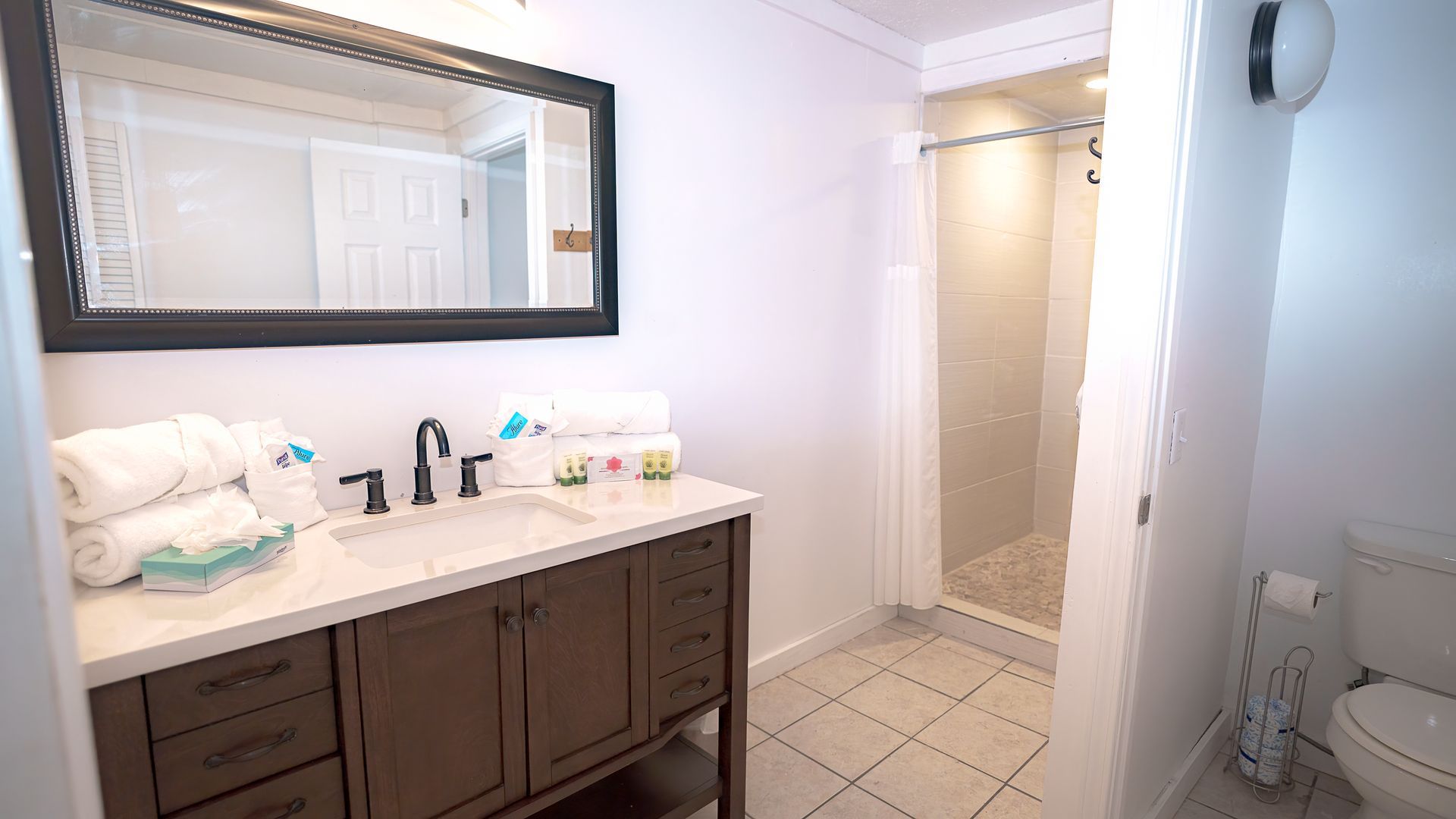 A bathroom with a sink , toilet , mirror and shower.